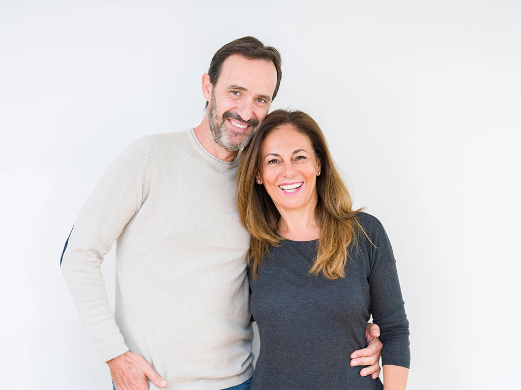 Smiling middle-aged couple showcasing restorative & surgical dental care results