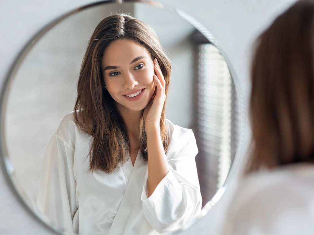 Woman admiring smile in mirror after Botox for TMJ & bruxism relief